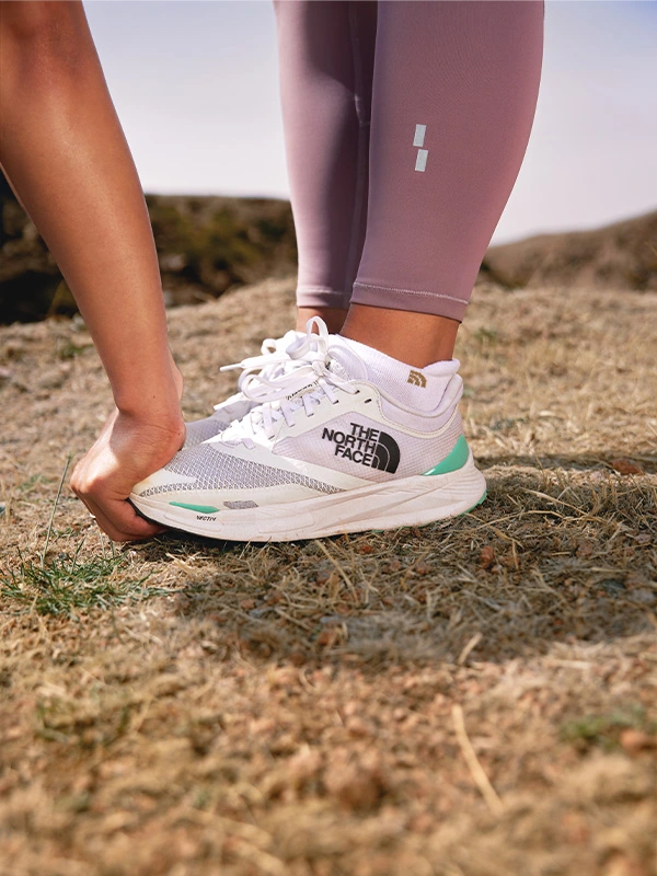 Runner tying a white VECTIV Enduris 3 shoe with mint details on a dry trail.