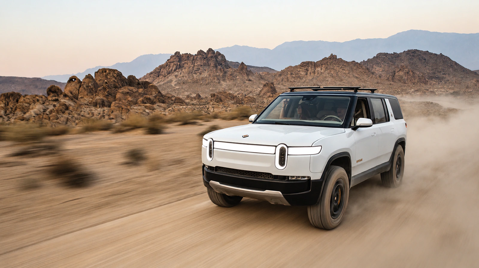 White Rivian R1S driving through a desert landscape.