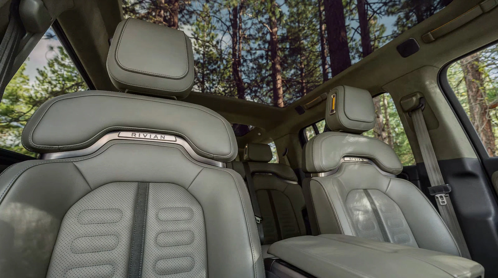 Rivian cabin showing sculpted front seats, panoramic glass roof and forest outside.