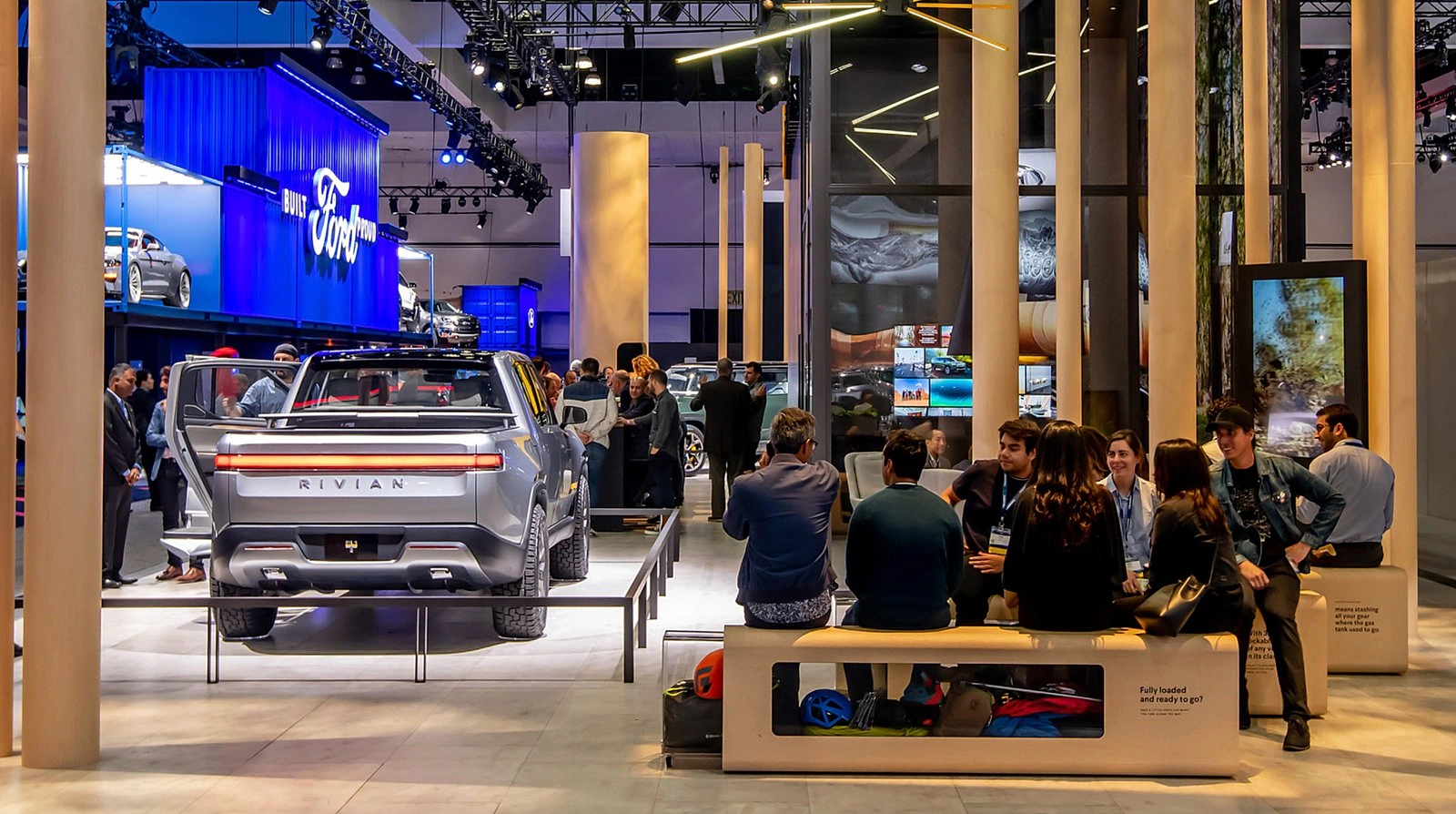 Visitors gathered around Rivian vehicles in an auto show environment.