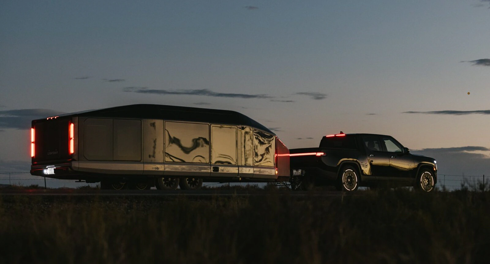 Lightship trailer being towed by a dark pickup at dusk.