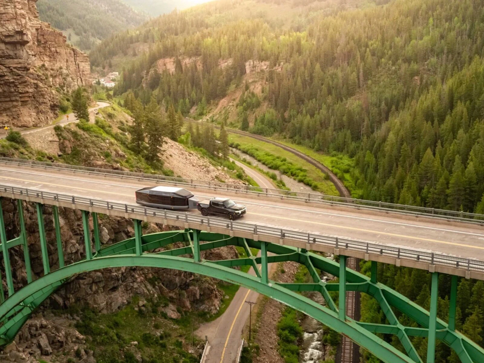 Lightship trailer and tow vehicle crossing a high green bridge through a mountain valley.