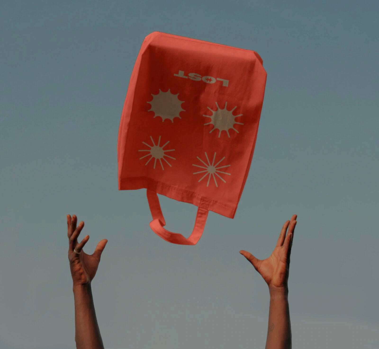 Red L.O.S.T. tote with illustrative travel symbols suspended against the sky.