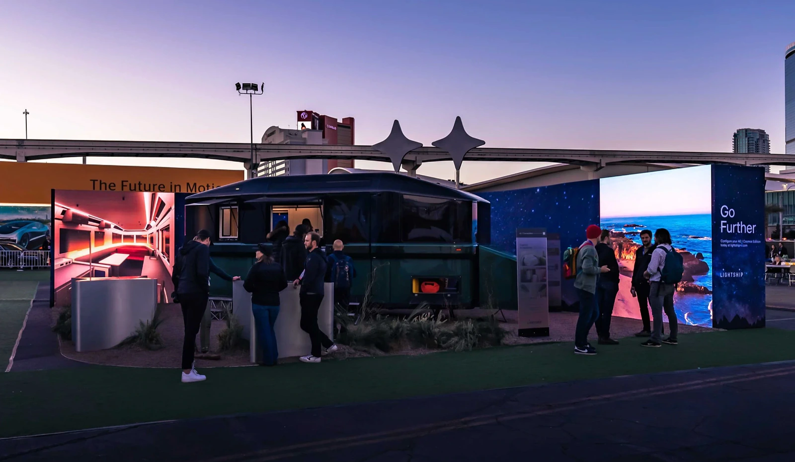 Front view of the Lightship CES display at dusk with illuminated exhibit graphics and visitors gathered around the trailer.