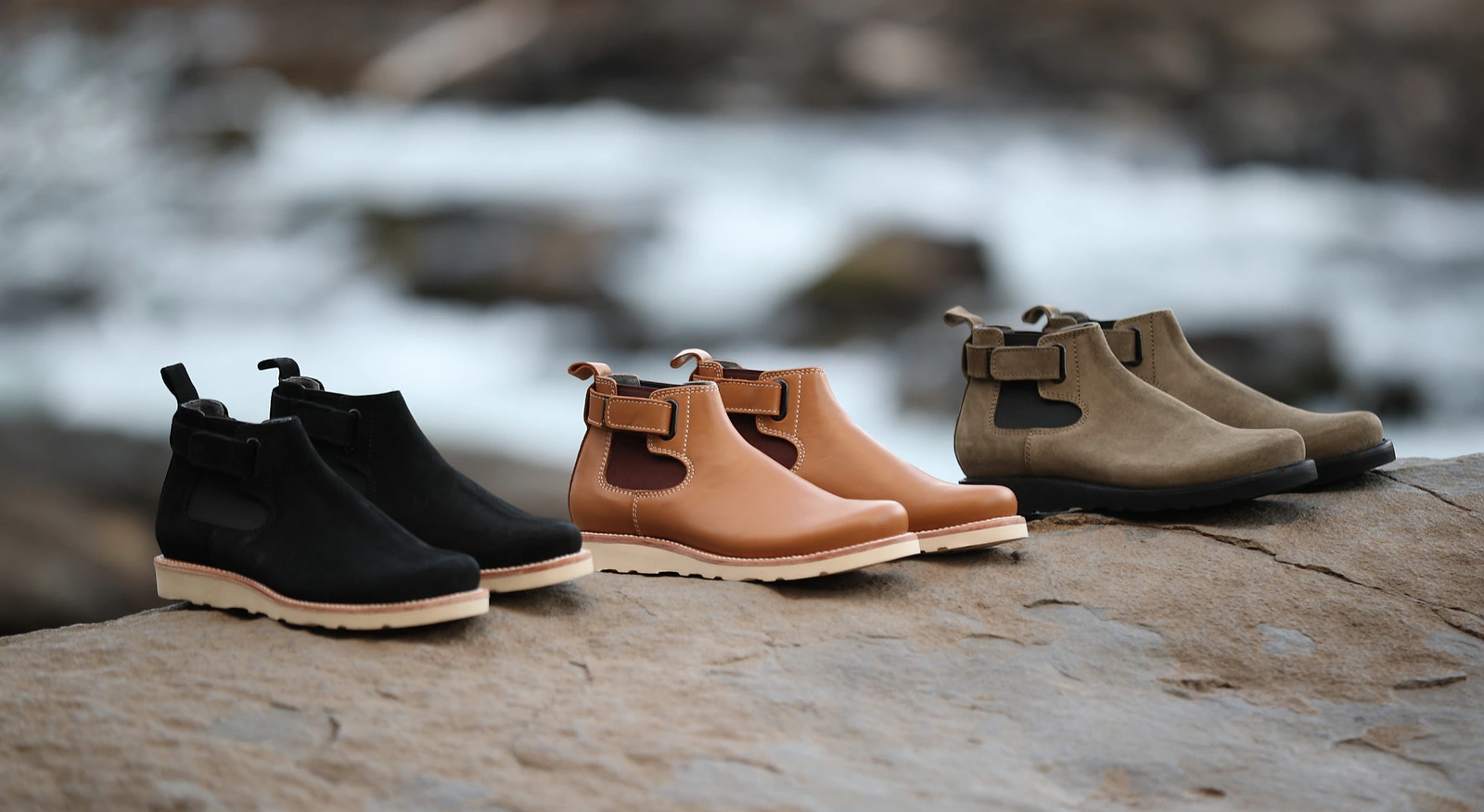 Three Terrascout ankle-boot color and material variants arranged on rock beside moving water.