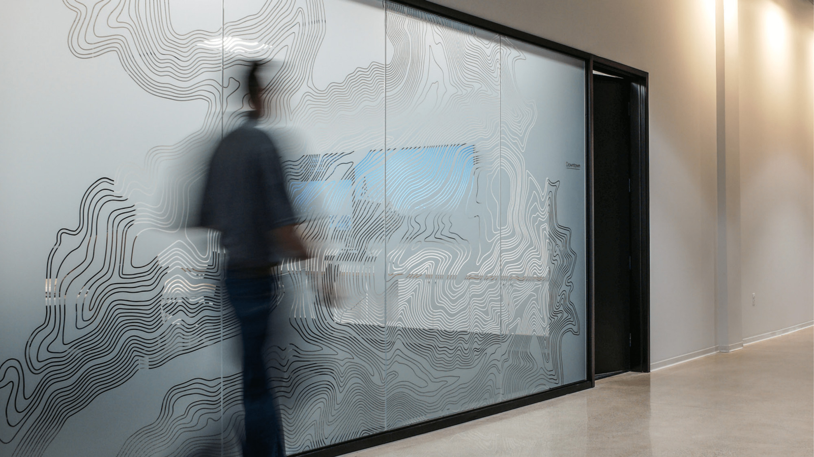 Topographic graphics across a glazed interior wall at Rivian’s Michigan headquarters.