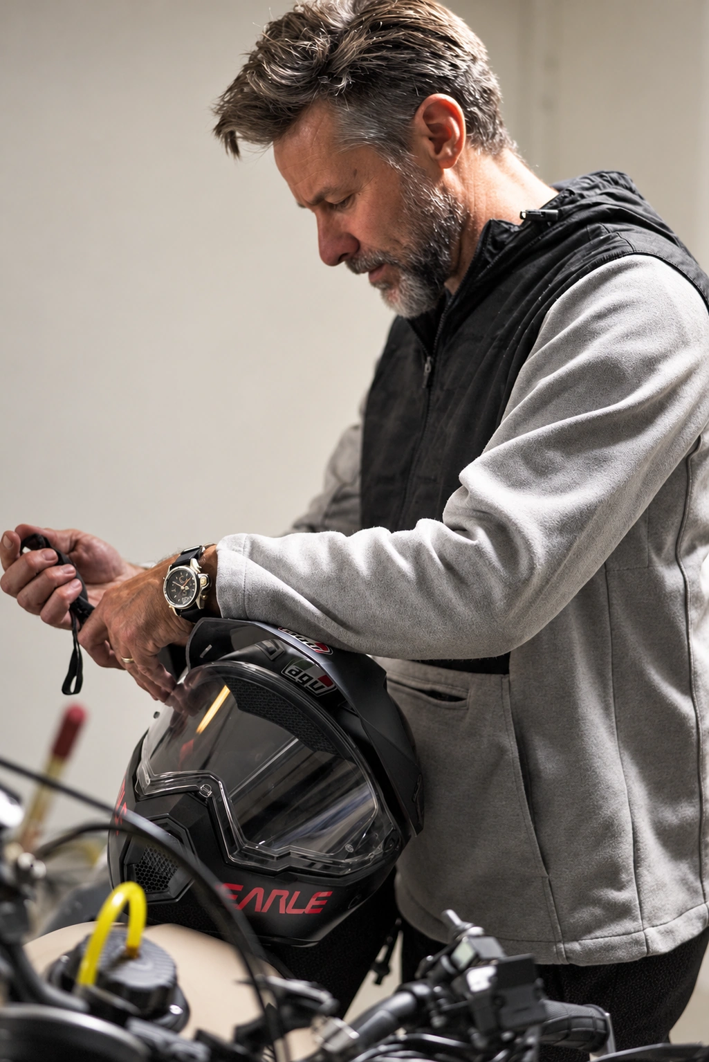 A man in the gray and black Terrascout anorak adjusts a motorcycle helmet strap, showing the garment’s fabric, panel construction and sleeve proportions.